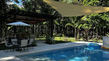 Een zwembad met een pergola en een terras met zitplaatsen.