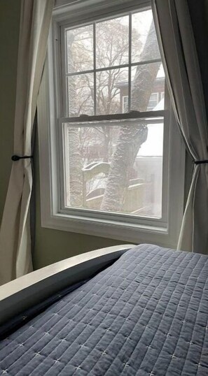 A bedroom with a window, a bed with a quilted cover, and curtains. - Sleepy Sanctuary (Evanston)