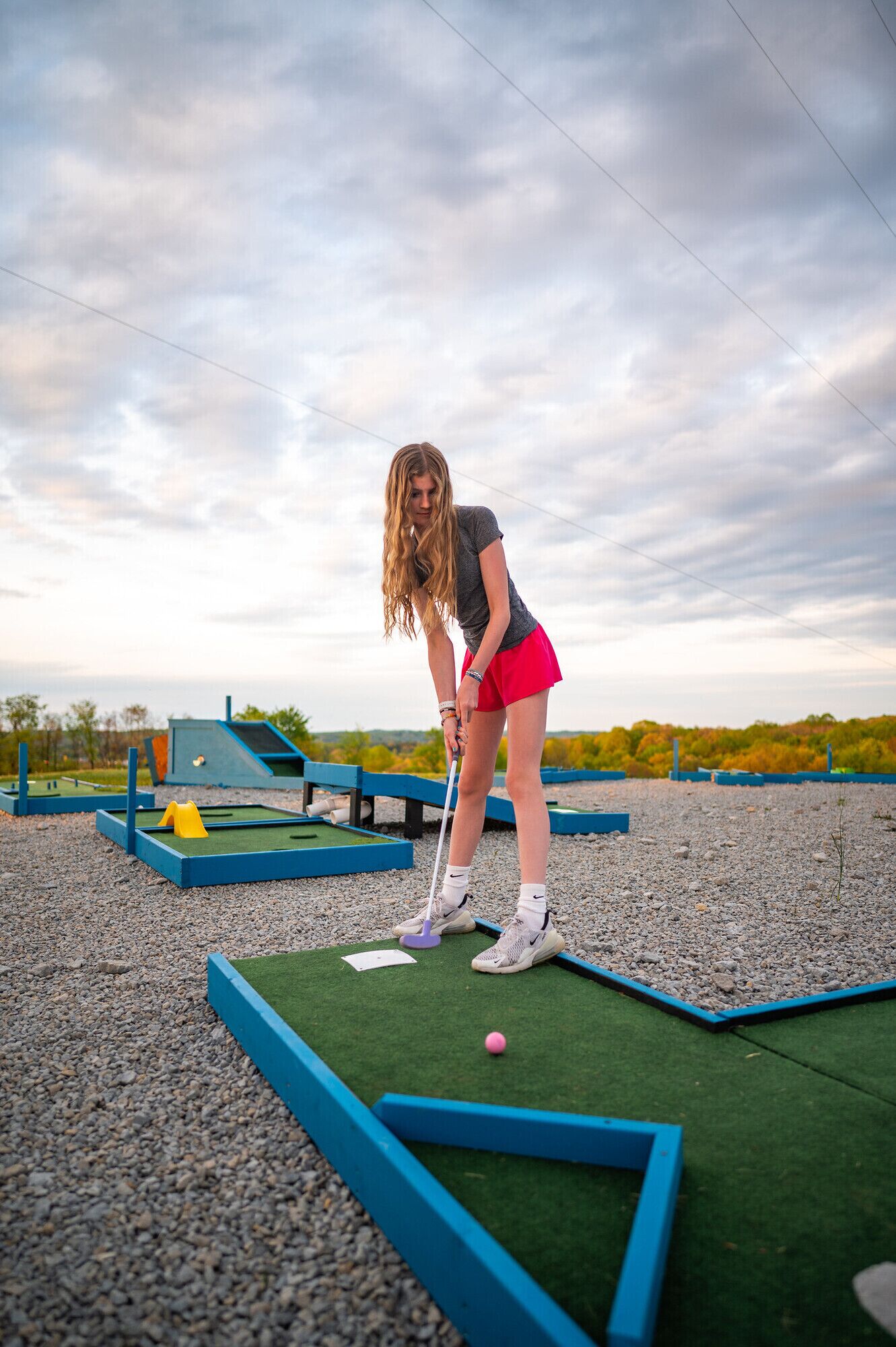 A person playing mini-golf on a green field with blue borders and a pink ball.