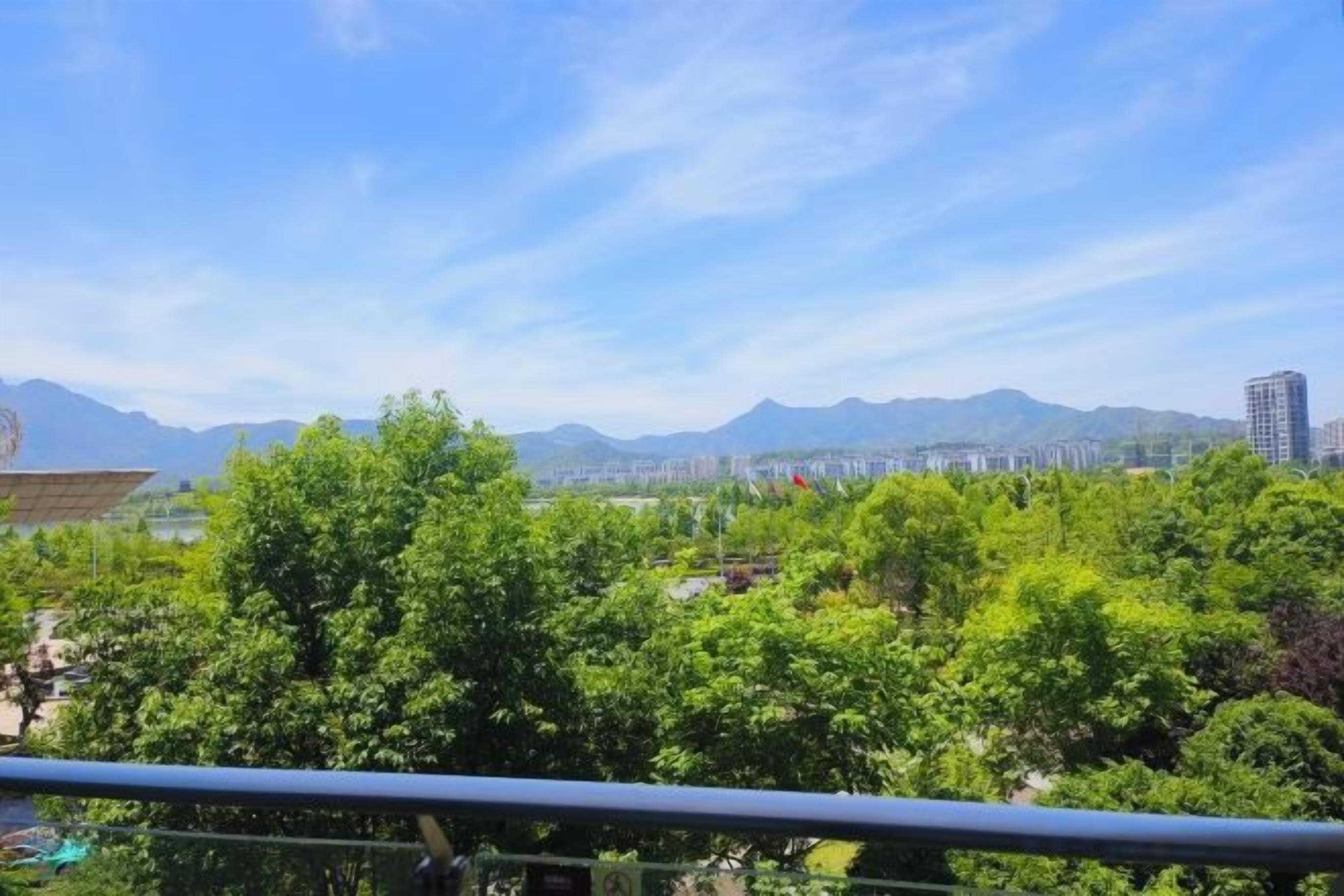 Vista d'una ciutat amb muntanyes al fons, cel serè i vegetació abundant al primer terme.