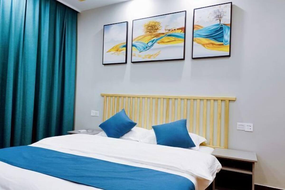Ein Schlafzimmer mit einem Bett, blau-weißer Bettwäsche, einem Holzkopfende und drei gerahmten Kunstwerken an der Wand.