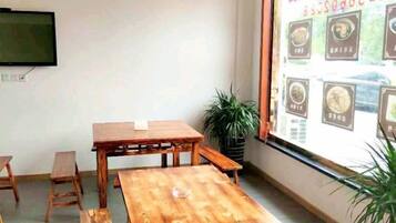 Una habitación con una mesa de madera, bancos, un televisor en la pared y un ventanal con carteleras de menú.