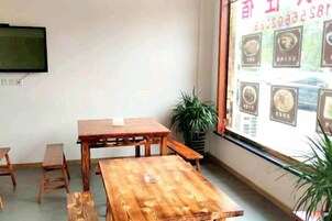 Una habitación con una mesa de madera, bancos, un televisor en la pared y un ventanal con carteleras de menú.