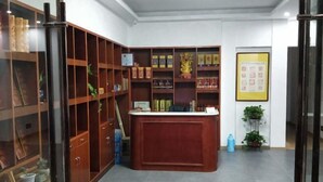 A reception area with a wooden desk, shelves with books and decorative items, and a framed poster on the wall. - Chen Xuan Yi Zhai (Jiu Hua Mountain Tourist Service Center Store) (Qingyang)