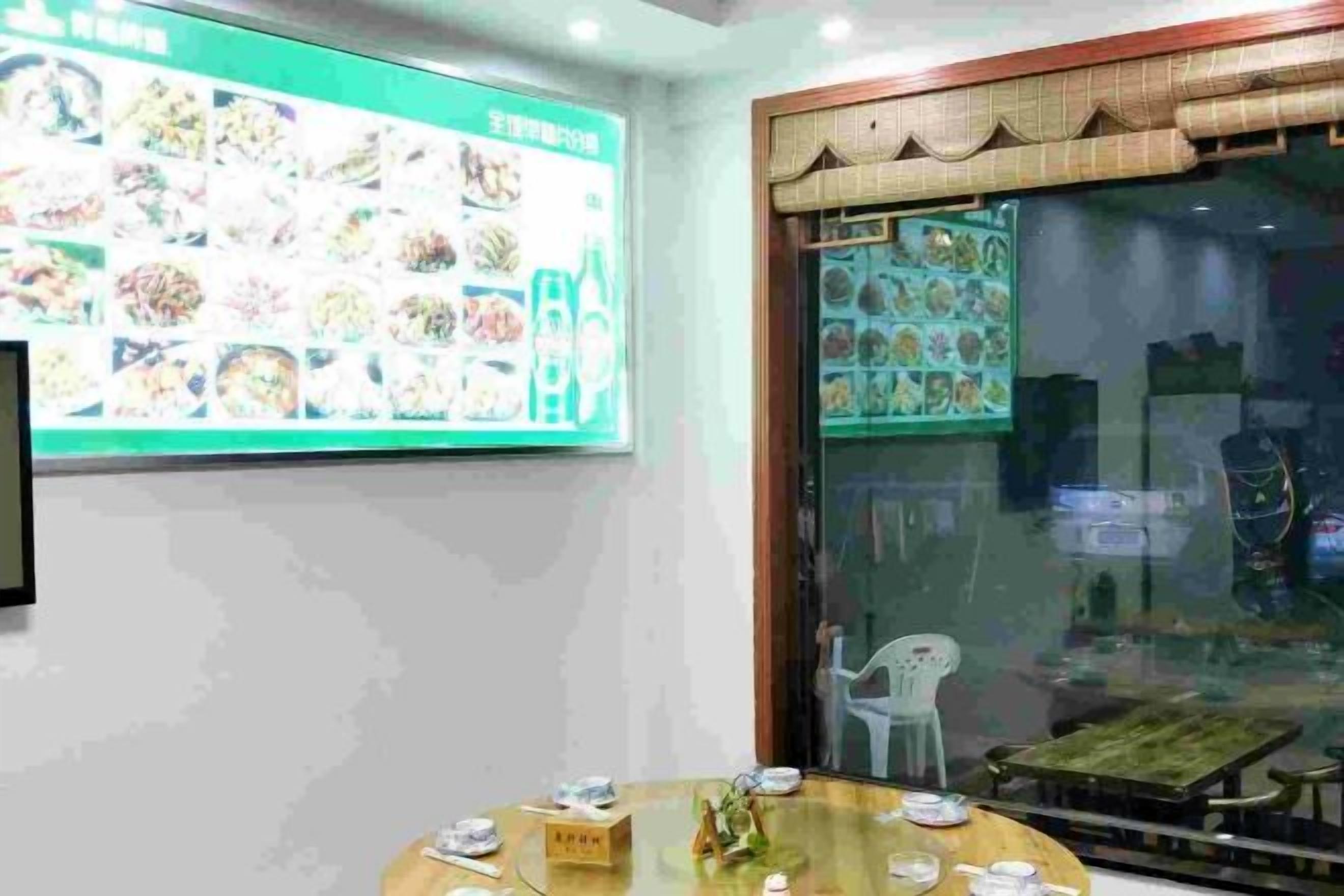 A dining area with a large menu display, a round table with plates and cutlery, and a view through a glass door.
