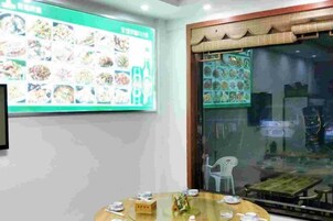 Un comedor con un gran cartel de menú, una mesa redonda con platos y cubiertos, y vista a través de un puerta de vidrio.