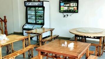 A room with wooden tables and benches, a refrigerator, and a television mounted on the wall.