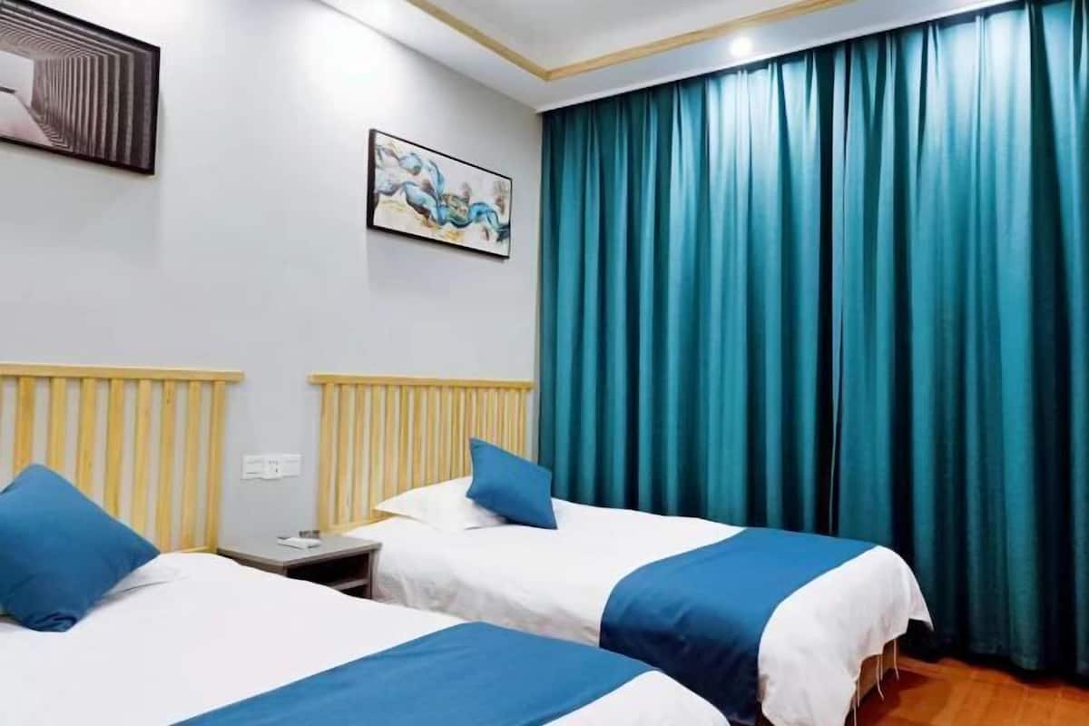 Ein Hotelzimmer mit zwei Betten, einem Bild an der Wand und einem großen Fenster mit Vorhängen.