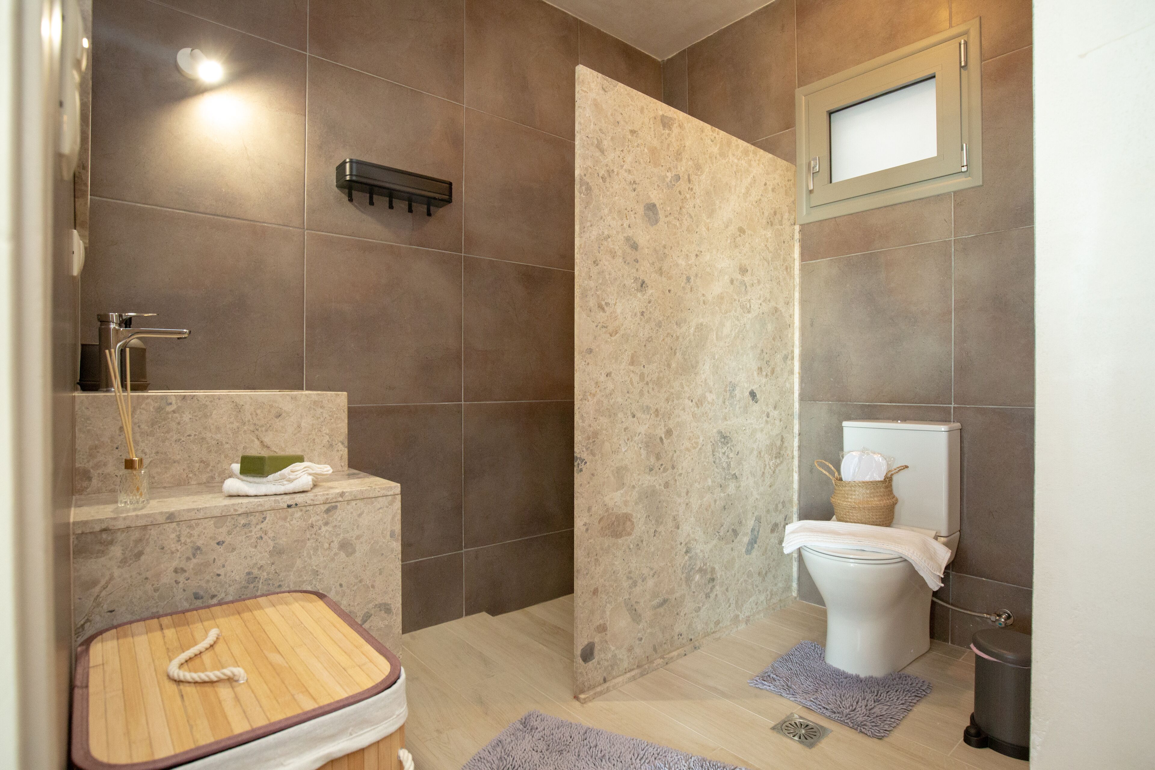 A bathroom with a shower, toilet, sink, and a small wooden stool.
