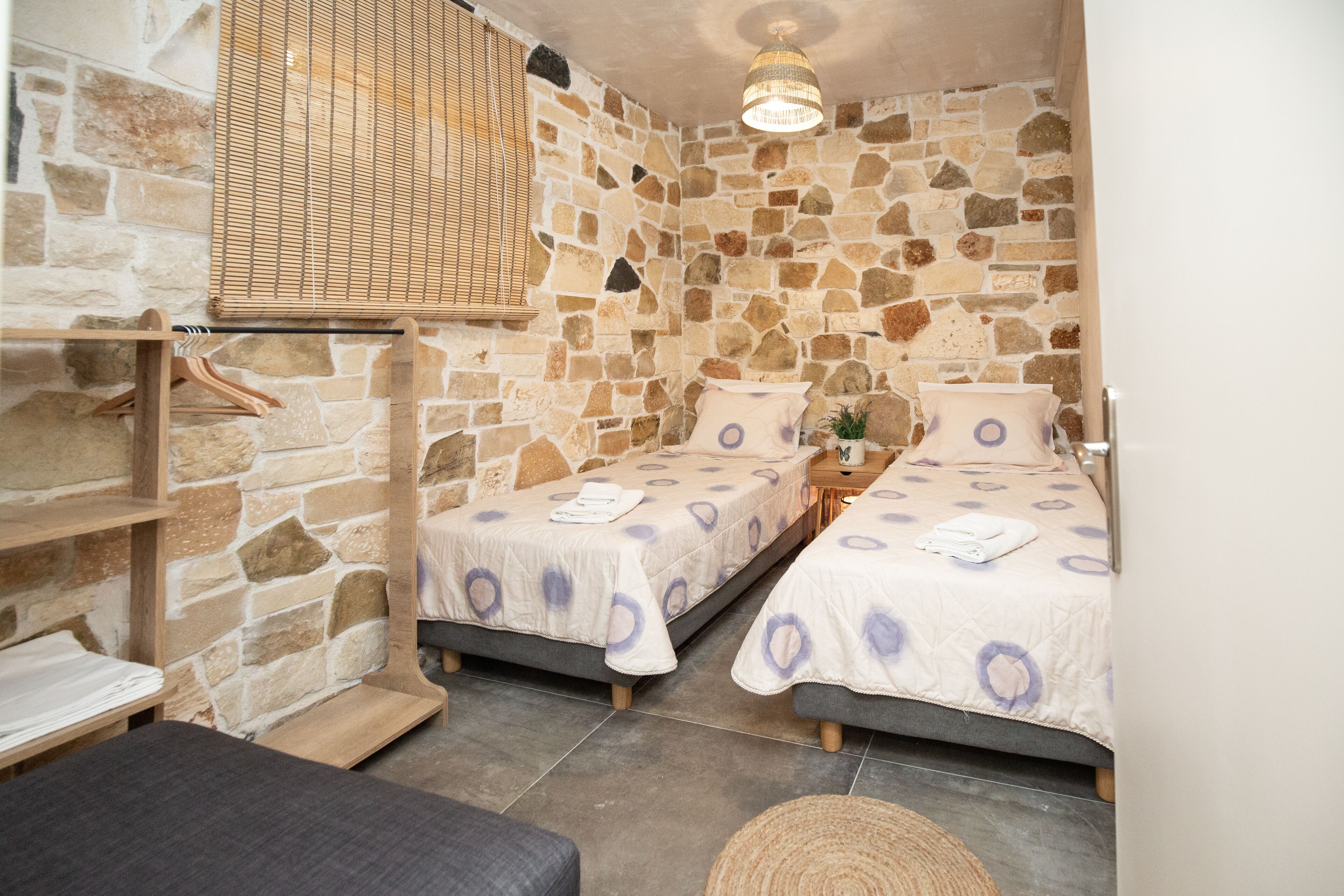 A cozy room with two beds, a wooden shelf, and a hanging light fixture.