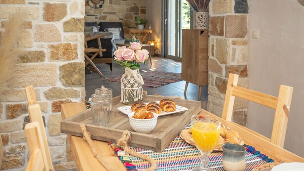 Ein Frühstückstisch mit Holzoberfläche, einer Vase mit rosa Rosen, Croissants und Orangensaft.