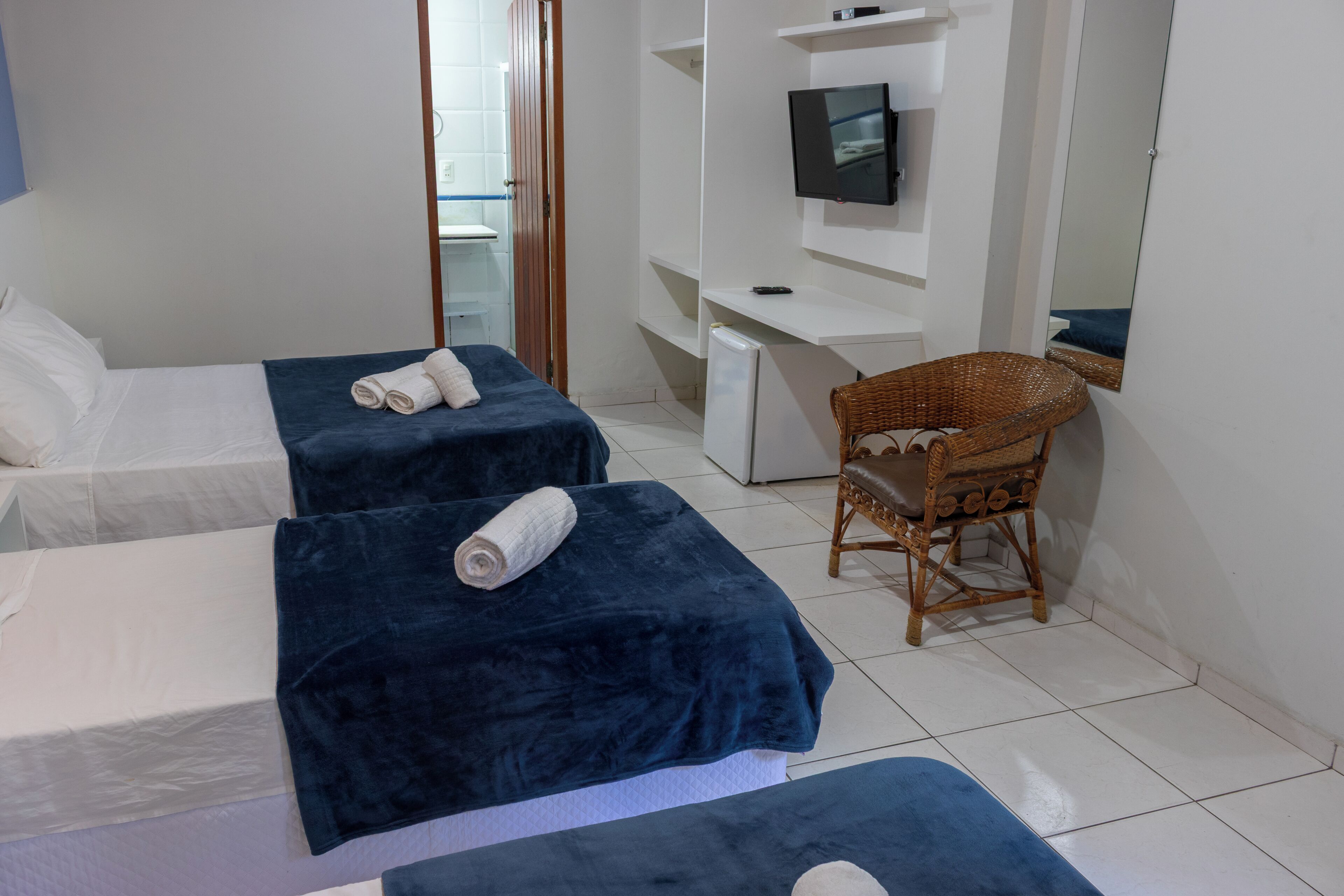 A hotel room with two beds, a desk, a chair, and a television.