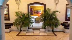 Un hall d’entrée avec un sol carrelé, un espace de repos central avec un fauteuil et deux plantes en pot.
