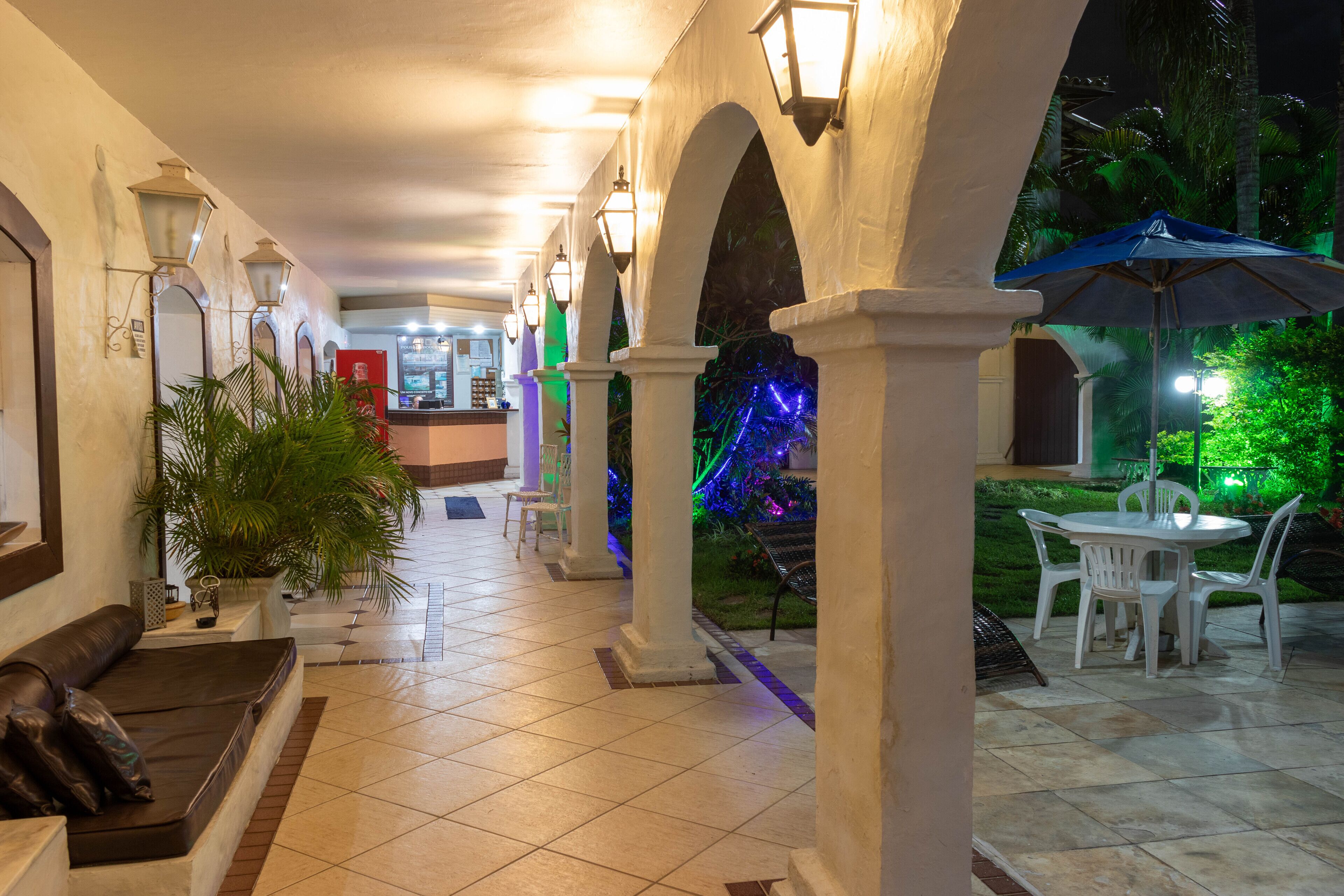 A hotel corridor with tiled flooring, white columns, and a seating area with a table and chairs.