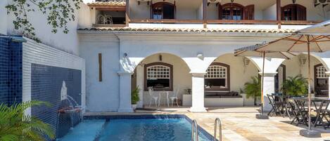 Un área de piscina con suelo de baldosas, fuente de agua y mobiliario de exterior.