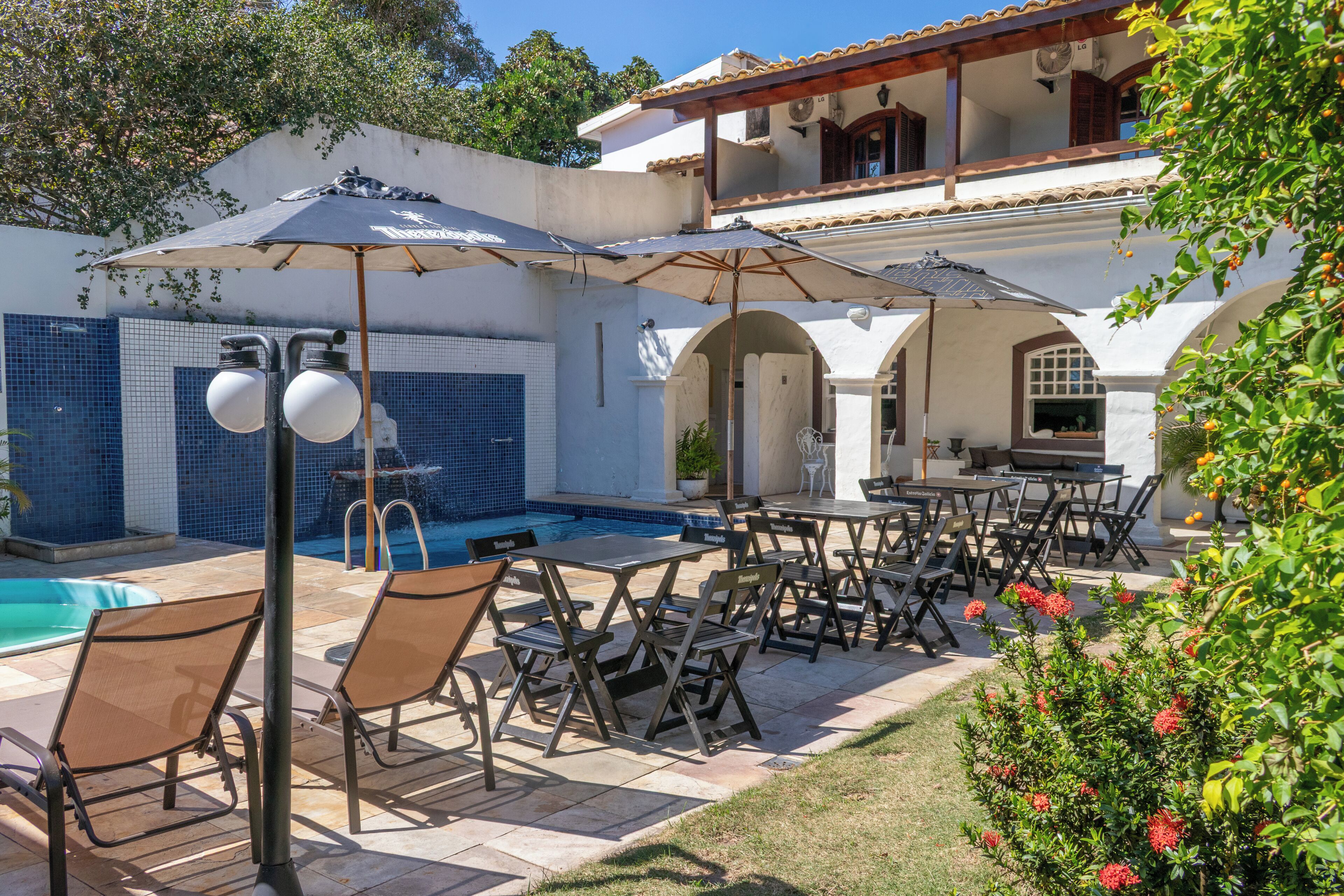 A poolside area with lounge chairs and umbrellas, a tiled pool, and a building with arches and a tiled roof.