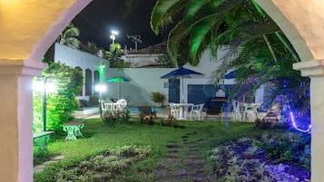 Un patio al aire libre bien iluminado con un sendero de piedra, mobiliario y abundante vegetación.