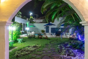 Un patio al aire libre bien iluminado con un sendero de piedra, mobiliario y abundante vegetación.