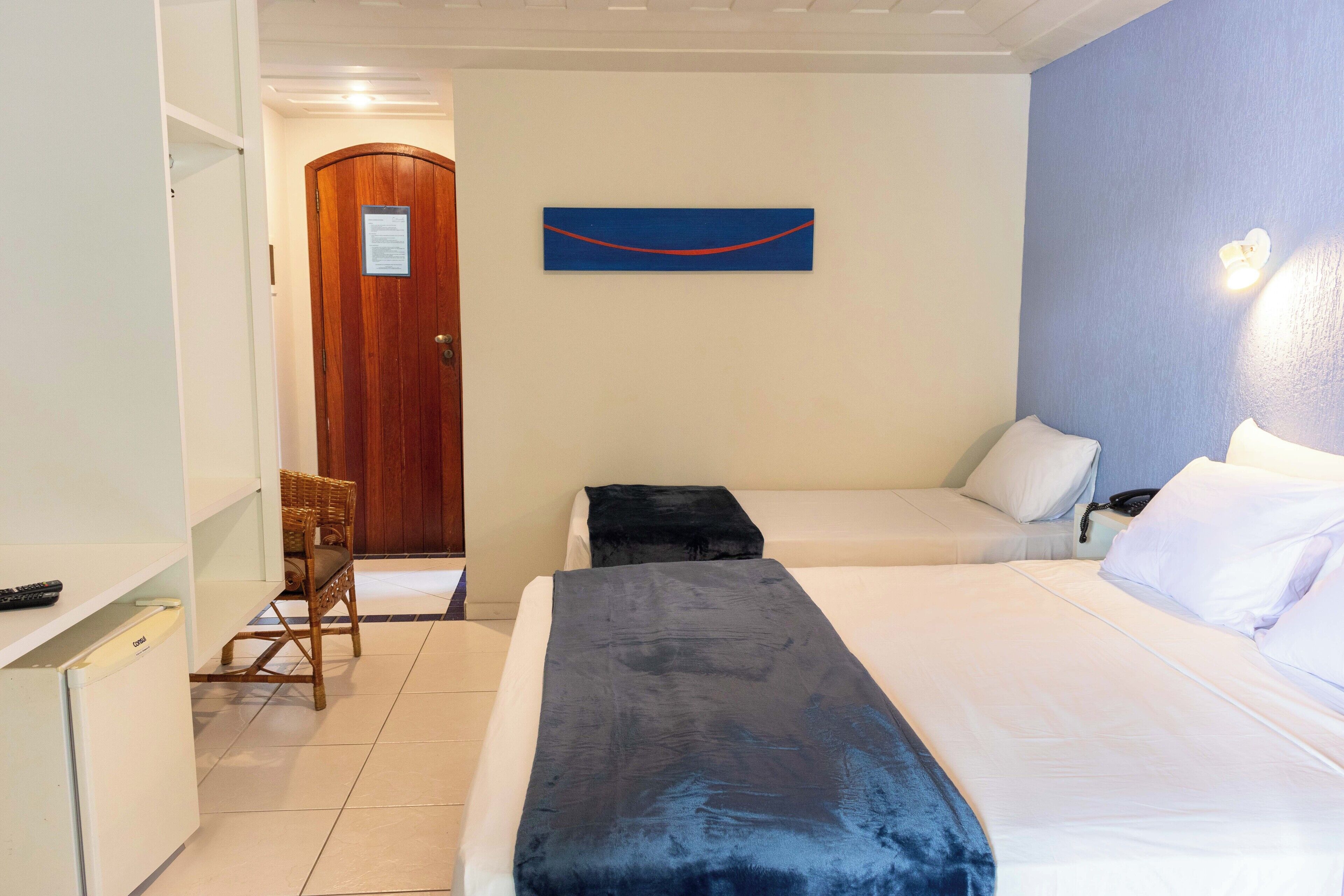 A hotel room with a bed, a chair, a desk, and a door.