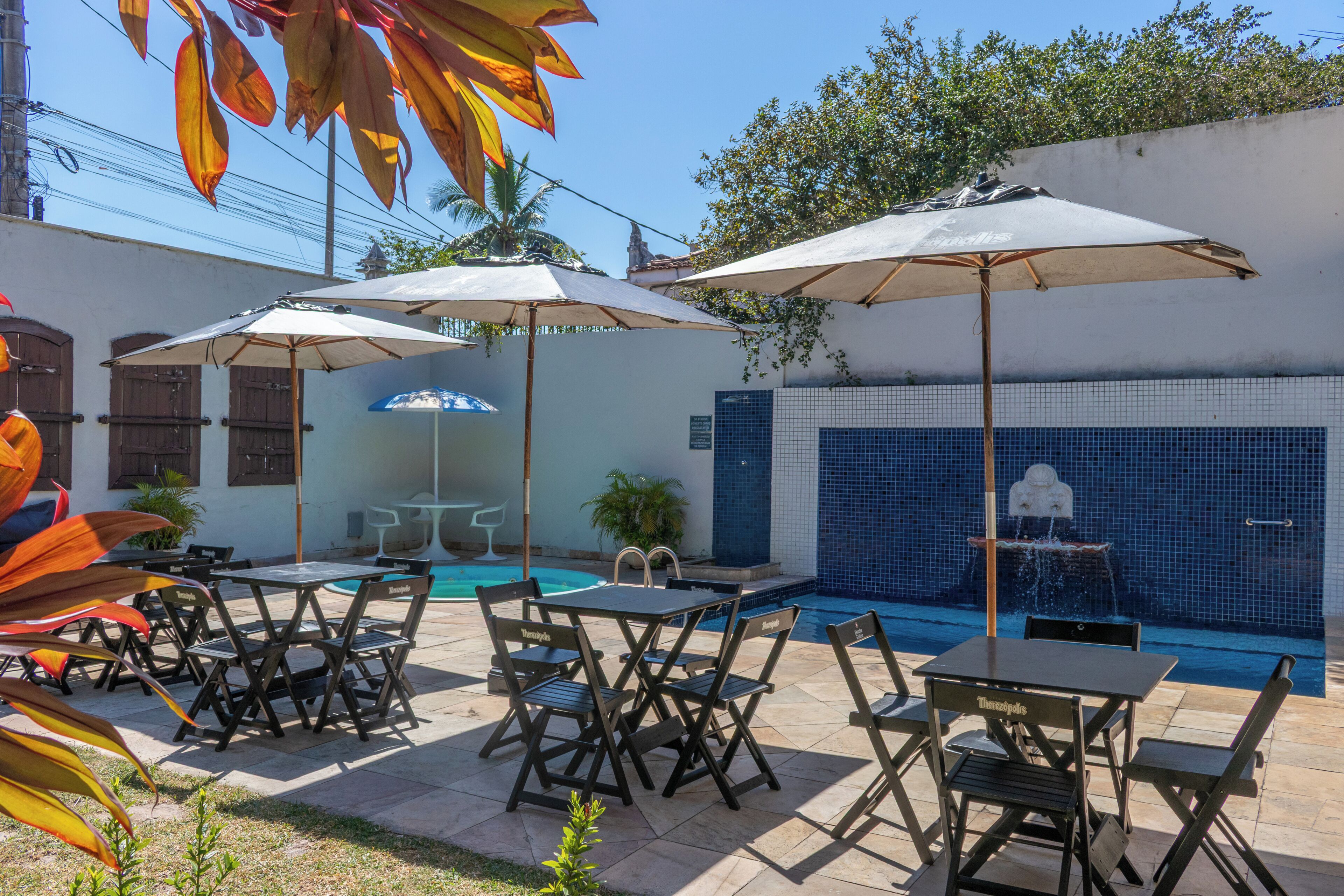 An outdoor patio area with tables and chairs, umbrellas, and a swimming pool in the background.