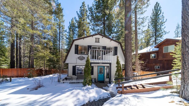A two-story lodge with a blue door and a balcony, surrounded by tall pine trees and a wooden fence. - Luna Lodge - 4BR, 2BA Close to Hike, Bike (South Lake Tahoe)