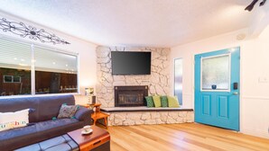 A living room with a stone fireplace, a blue door, and a black leather sofa. - Luna Lodge - 4BR, 2BA Close to Hike, Bike (South Lake Tahoe)
