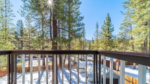 A wooden deck with a view of a snowy landscape and tall pine trees. - Luna Lodge - 4BR, 2BA Close to Hike, Bike (South Lake Tahoe)