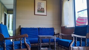 Een kamer met een houten bank en stoelen, een kleine tafel en een raam met uitzicht op bomen.