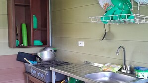 Een kleine keuken met een gasfornuis, spoelbak en een groene gasfles.