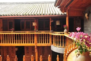 A traditional wooden building with a tiled roof, a wooden balcony with railings, and a large vase with flowers. - Moonshine Inn (Dali City)