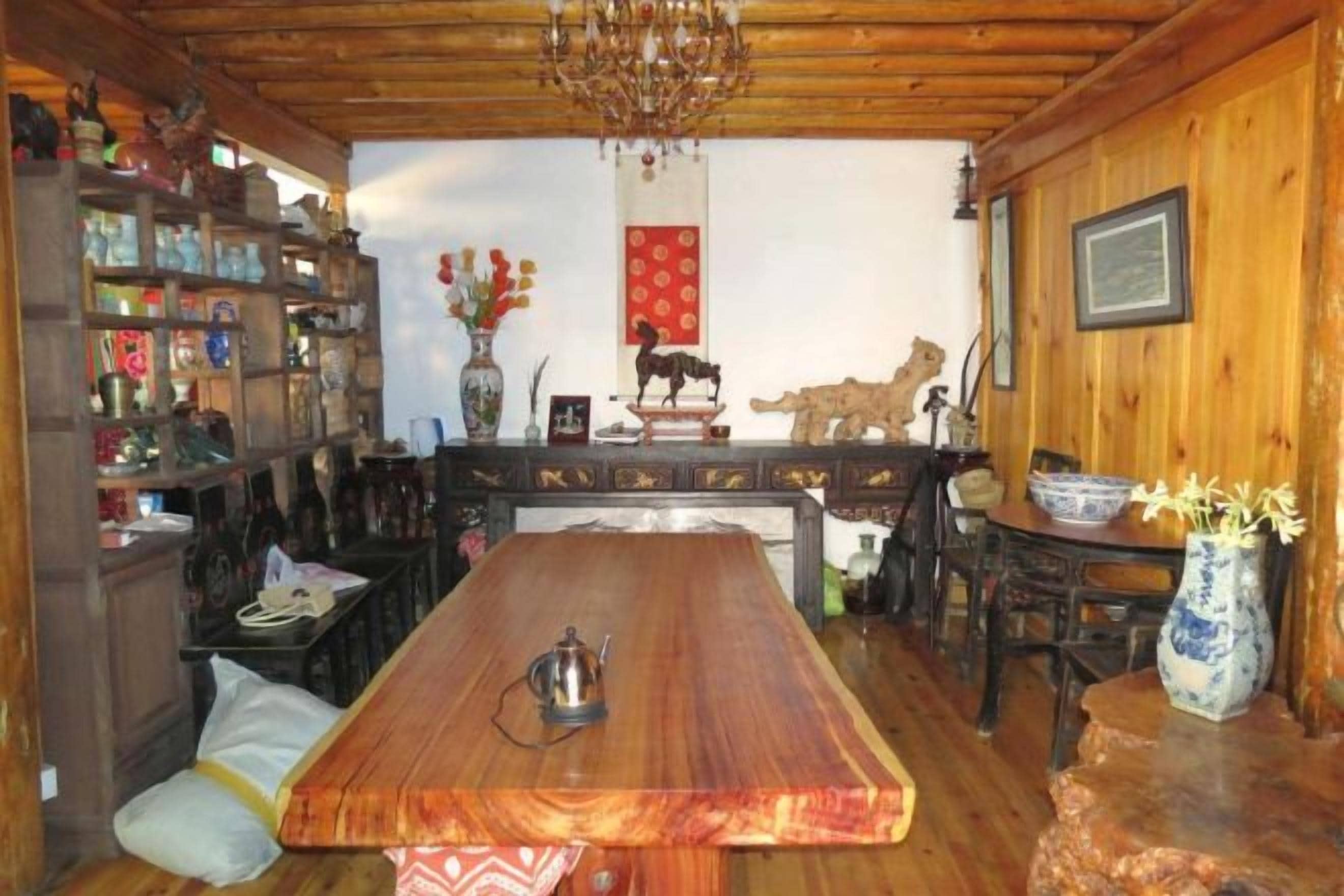 Un comedor de madera con una mesa larga, sillas, una lámpara de araña y una estantería llena de objetos diversos.