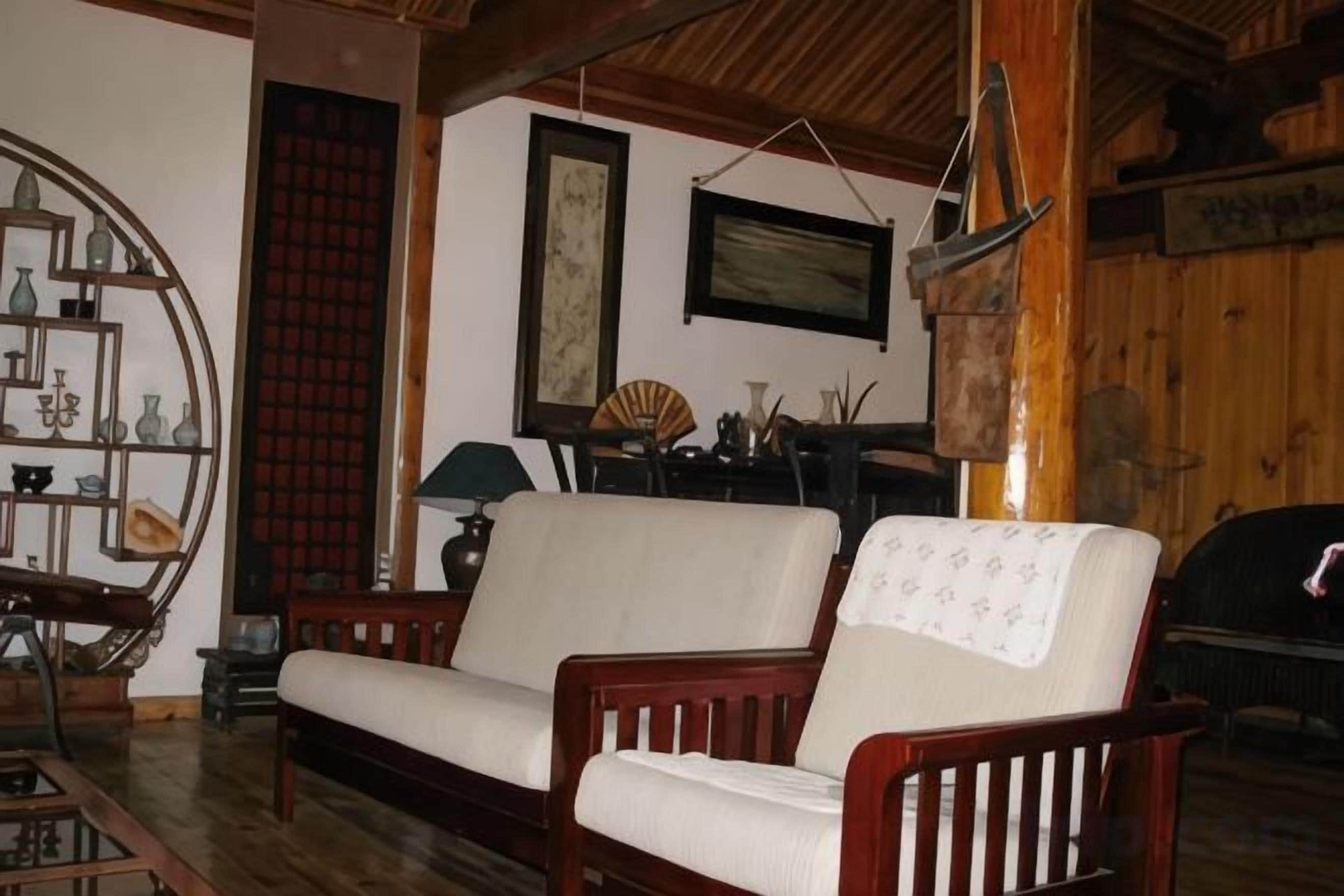Una habitación con un sofá de madera, una mesita auxiliar, una lámpara y un estante con adornos.