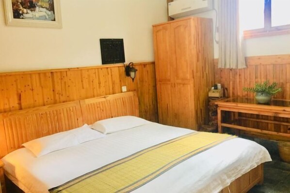 Ein Zimmer mit Holzwandverkleidung, einem Bett, einem Holzschrank, einem kleinen Tisch mit Pflanze und einer Wandleuchte.