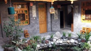 A courtyard with a stone pathway, potted plants, a small pond, and wooden furniture. - Moonshine Inn (Dali City)