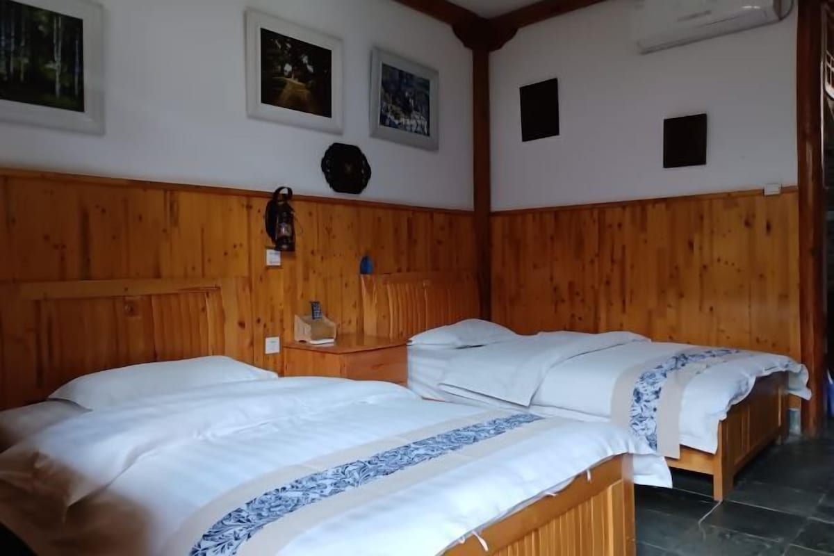 Ein Zimmer mit zwei Holzbetten, einem Holz-Kopfteil, einem kleinen Nachttisch mit Lampe und gerahmten Bildern an der Wand.