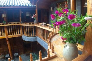 A wooden balcony with a railing, a vase with flowers, and a traditional tiled roof. - Moonshine Inn (Dali City)