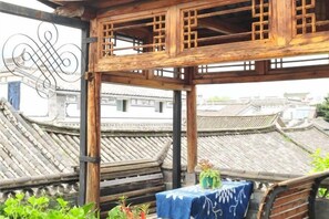 A traditional wooden pavilion with a table and plants, overlooking a cityscape with tiered rooftops. - Moonshine Inn (Dali City)