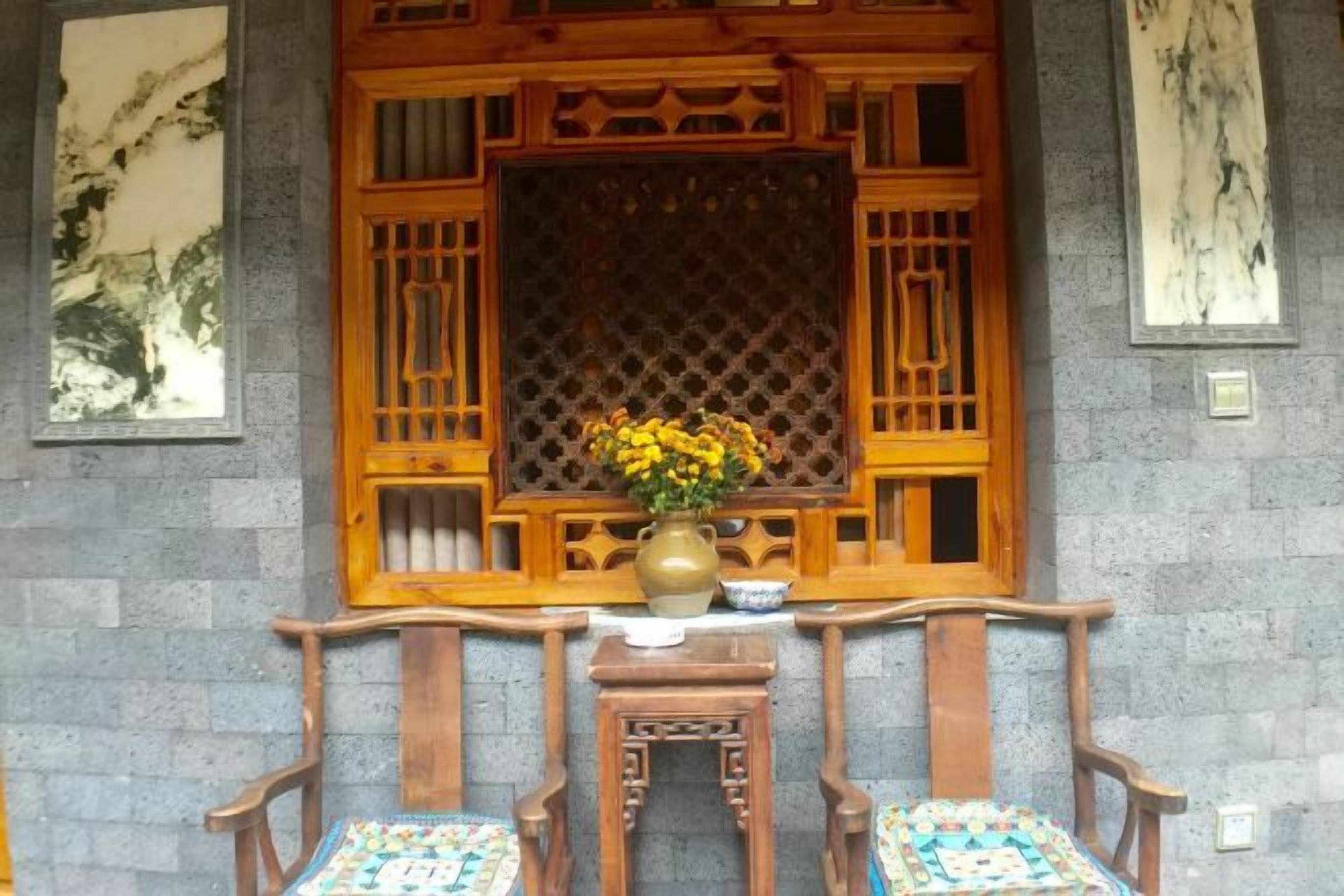 A traditional Chinese window with wooden lattice, a vase with yellow flowers, and two wooden chairs with patterned cushions.