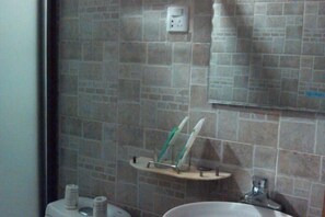 Ein Badezimmer mit Wand aus Steinplatten, einem Spiegel, einem Waschbecken und einer Zahntenspenstermann.