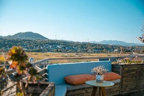 A rooftop terrace with a view of a distant town and hills, a blue sofa, and a small round table with a vase. - Qingtian Yashe Inn (Tengchong)