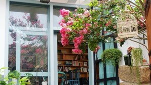 A cozy reading nook with a large window, a bookshelf, and a hanging birdcage. - Qingtian Yashe Inn (Tengchong)