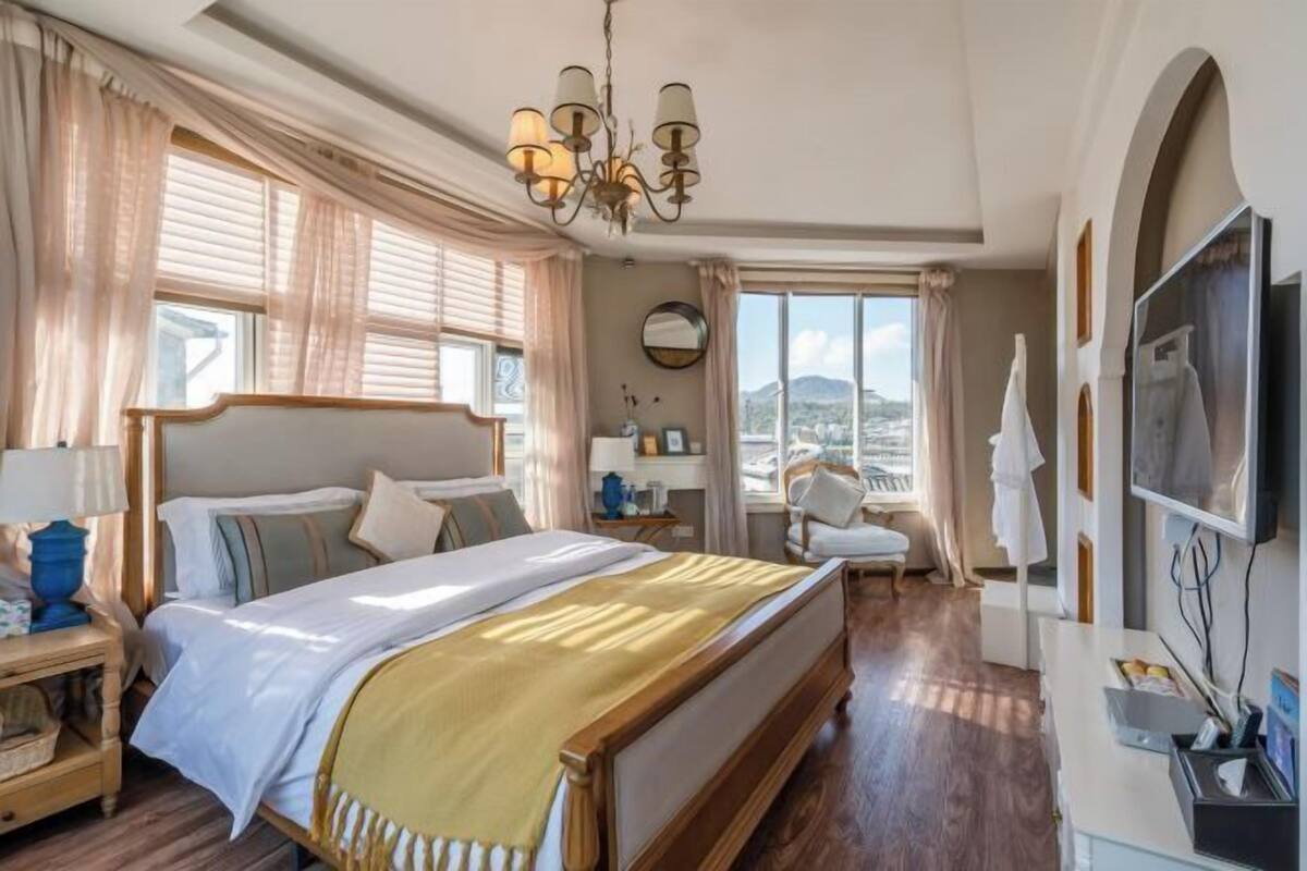 Habitación de hotel con una cama grande, un candelabro, un televisor y vista a la ciudad.