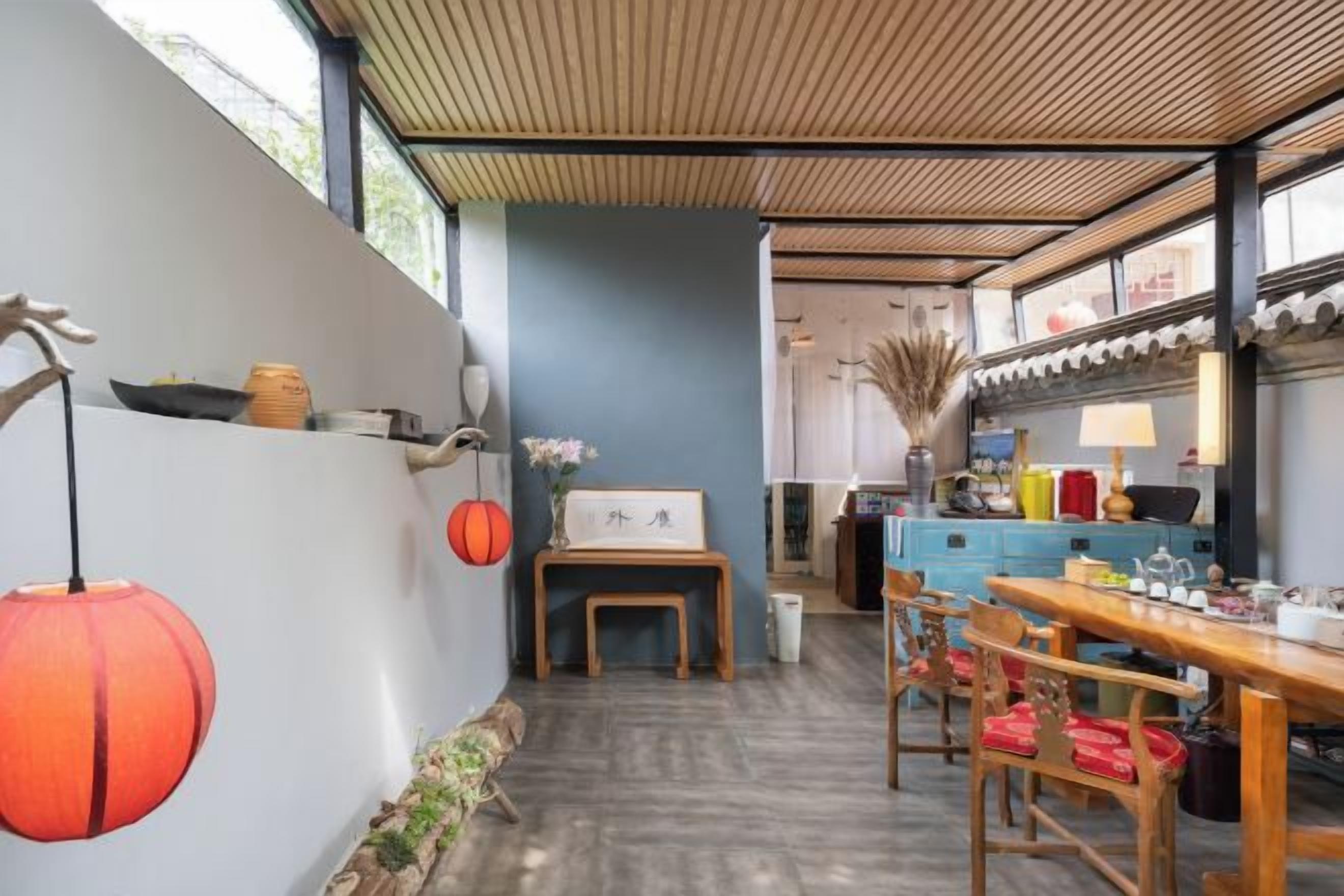 A room with a wooden ceiling, a dining table with chairs, a small table with a vase, and a wall with decorative items.