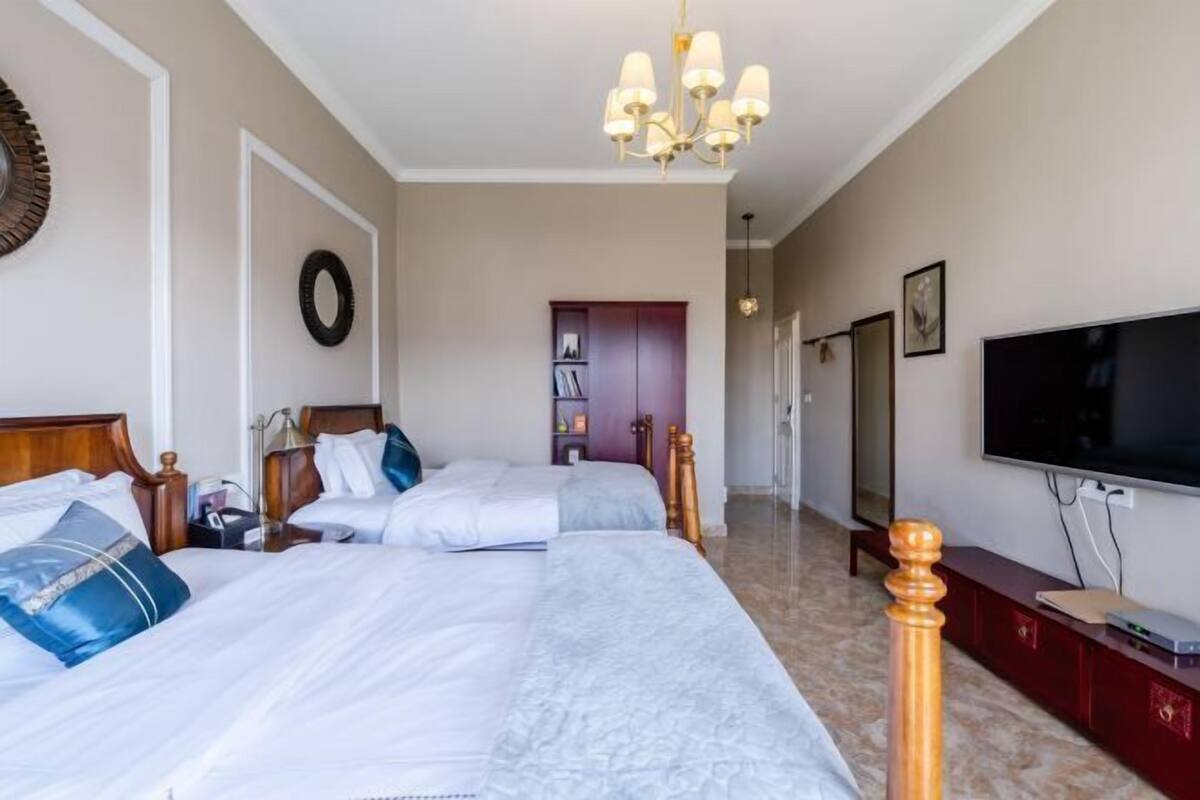 Una habitación de hotel con dos camas, televisión, candelabro y aparador de madera.