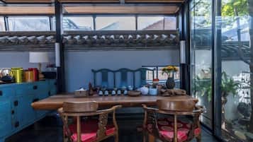 A dining area with a wooden table and chairs, a blue cabinet, and a view through large windows.