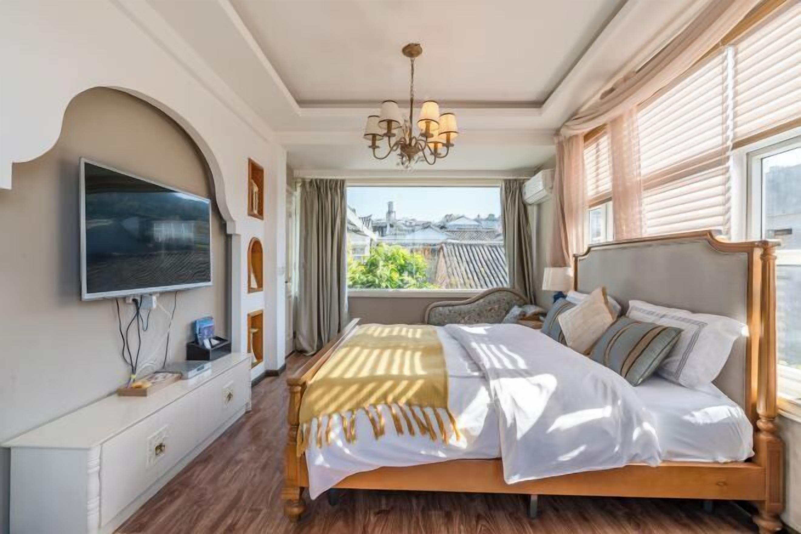 Quarto de hotel com cama, TV fixada na parede, cómoda de madeira e vista para a cidade pela janela.