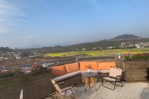 A terrace with a wooden bench, a small table, and a view of a green landscape with buildings in the distance. - Qingtian Yashe Inn (Tengchong)