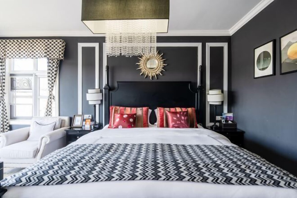 Ett modernt hotellrum med en stor säng, en kristallkrona, en solformad spegel och en randig gardinkappa.