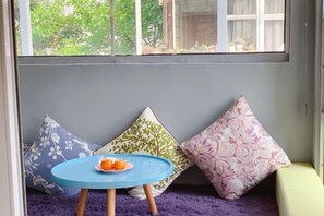 A cozy seating area with a round table and a tray of oranges, surrounded by floral-patterned cushions. - Qingtian Yashe Inn (Tengchong)