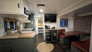 A compact RV interior with a kitchenette, a dining area, and a seating space. - Modern Vintage Camper w/ Peaceful Private Yard (Eugene)